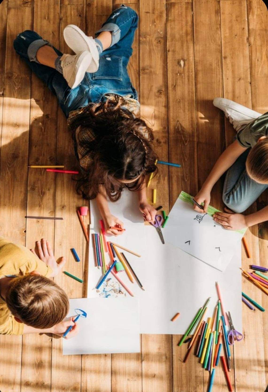 Enfants qui dessinent et découpent au sol, vus d’en haut